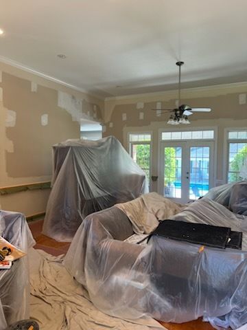 Living room under renovation, furniture covered in plastic sheets and paint patches on the walls.