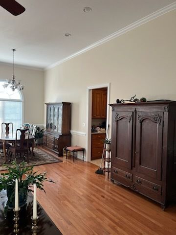 Bright dining room with hardwood floors, dark wood cabinet, chandelier, and large window by a dining table