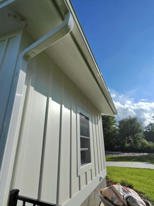 White-sided house exterior with a gutter, window, and grassy yard under a blue sky