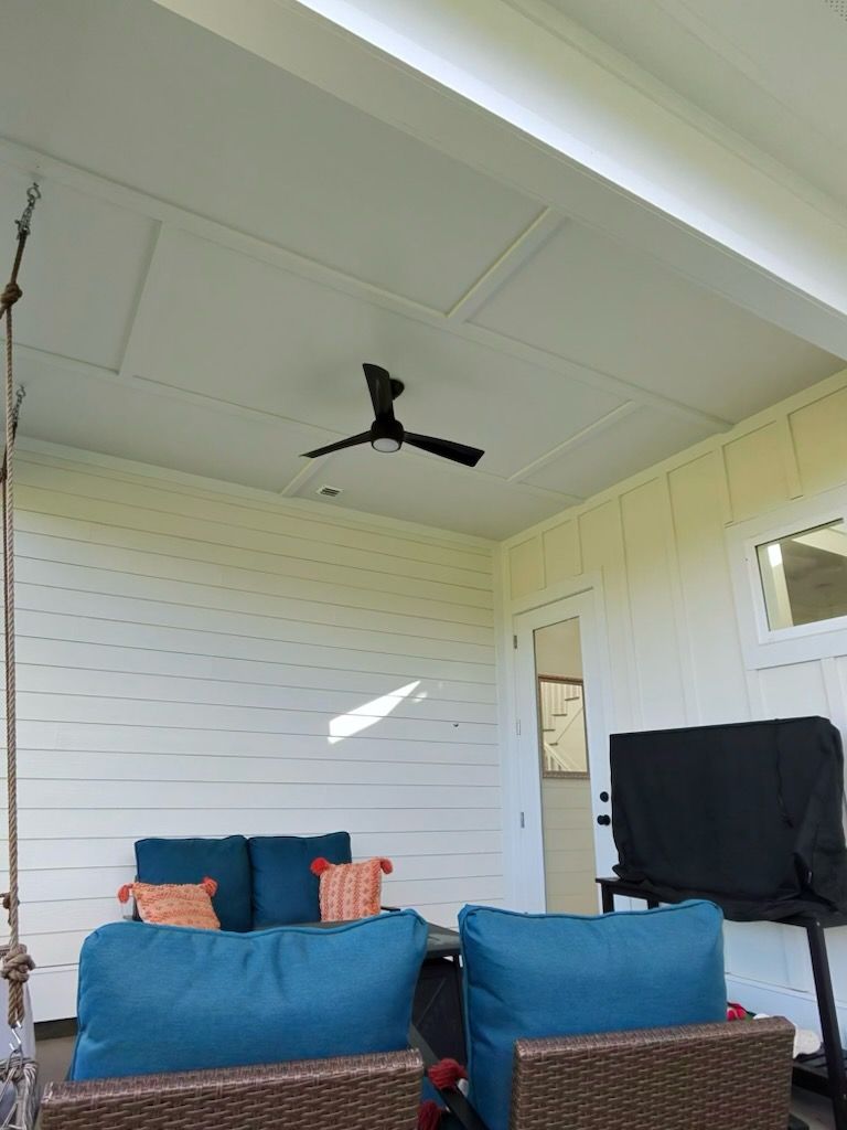 Screened porch with blue chairs, white beadboard walls, and a black ceiling fan