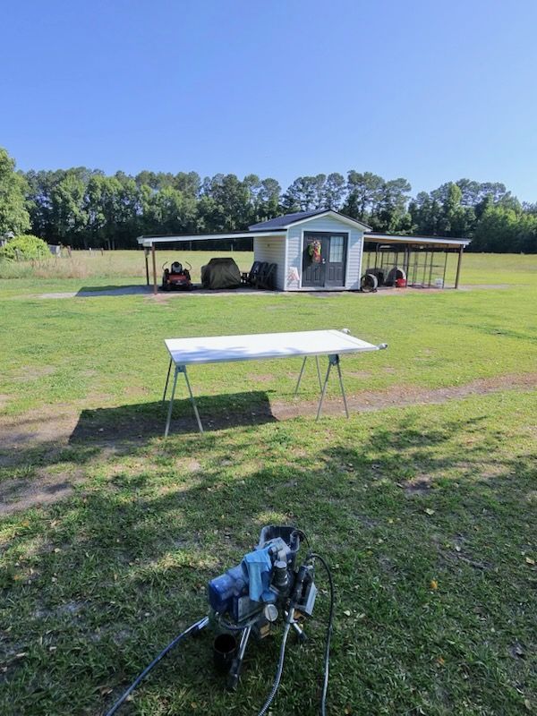 Open grassy field with a small shed, covered equipment area, white table, and a robot in the foreground