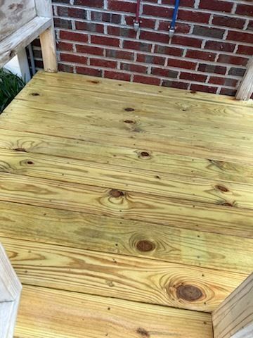Wooden deck platform beside a brick wall, viewed from above.