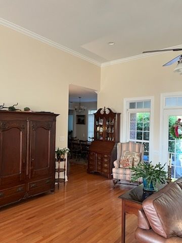 Spacious living room with hardwood floors, wooden furniture, and glass doors opening to greenery.