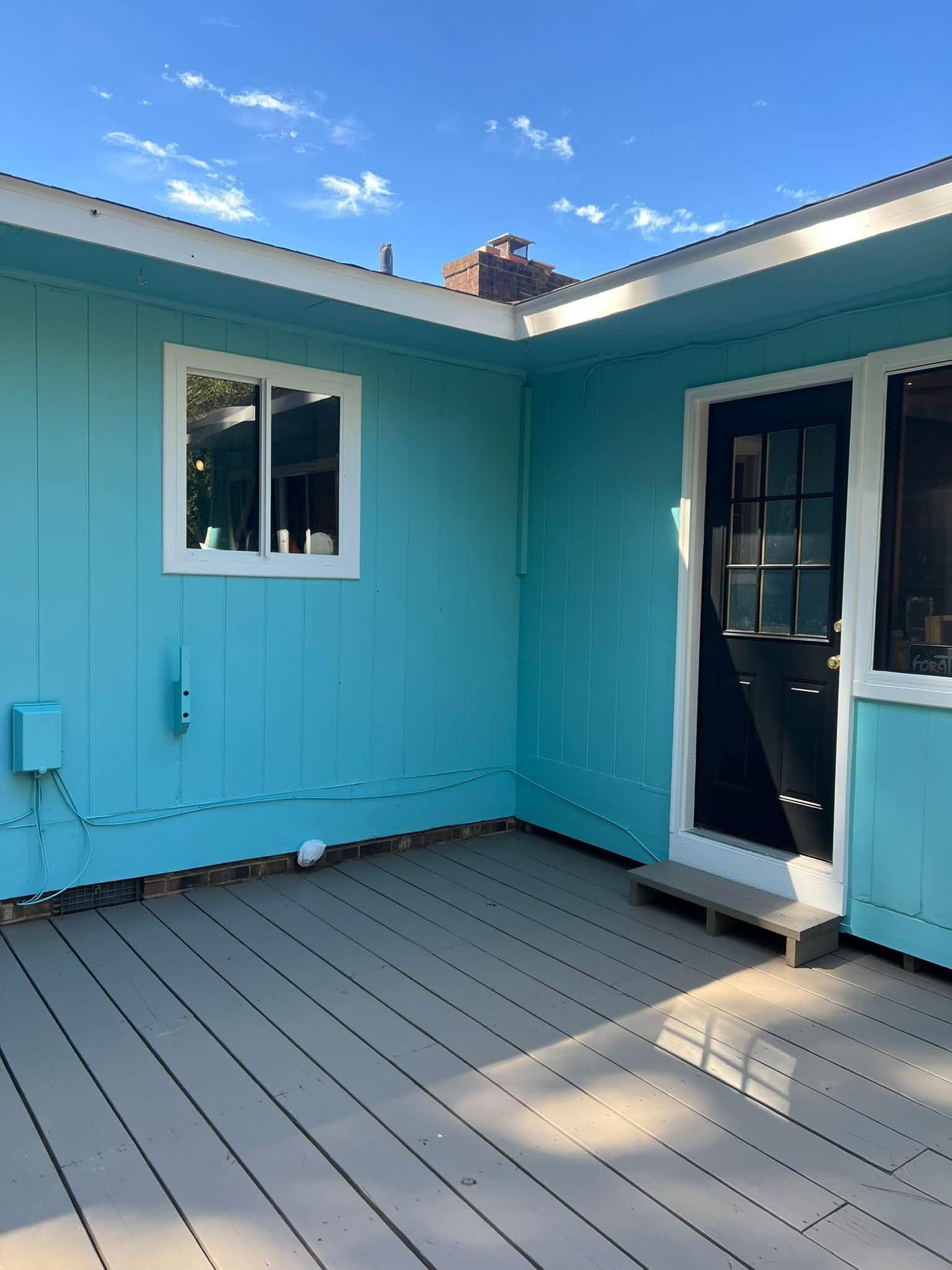 Turquoise patio with gray deck, window, and open glass door under a blue sky