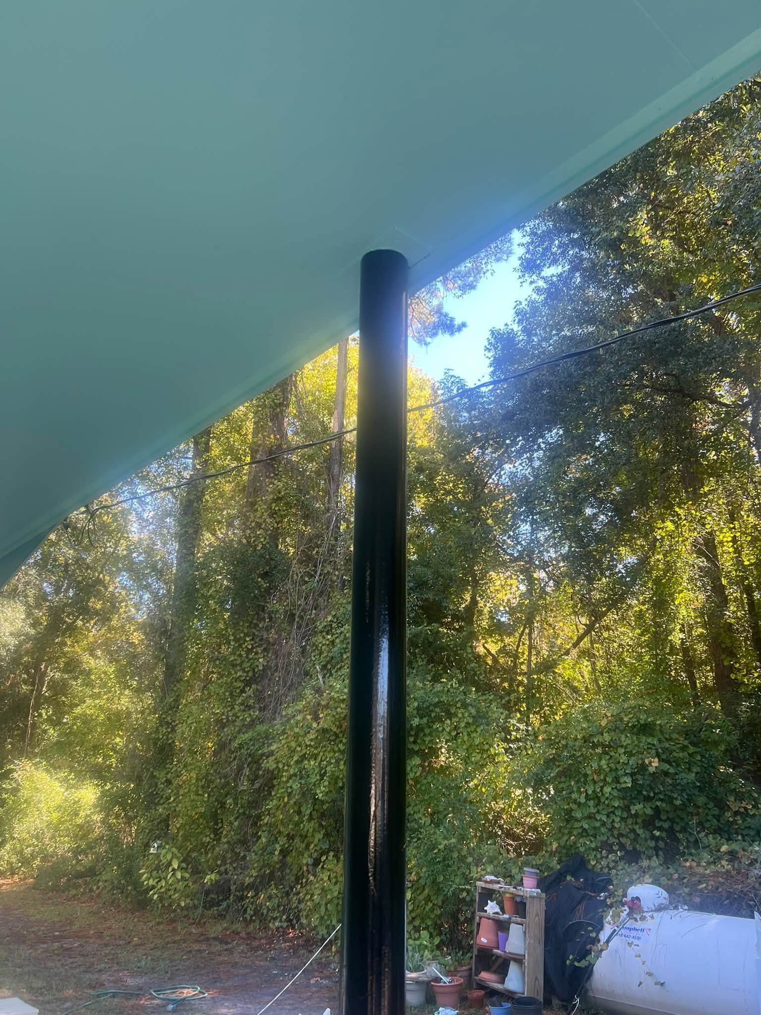Outdoor patio with a dark support pole, trees, and bright sunlight beyond the roofline