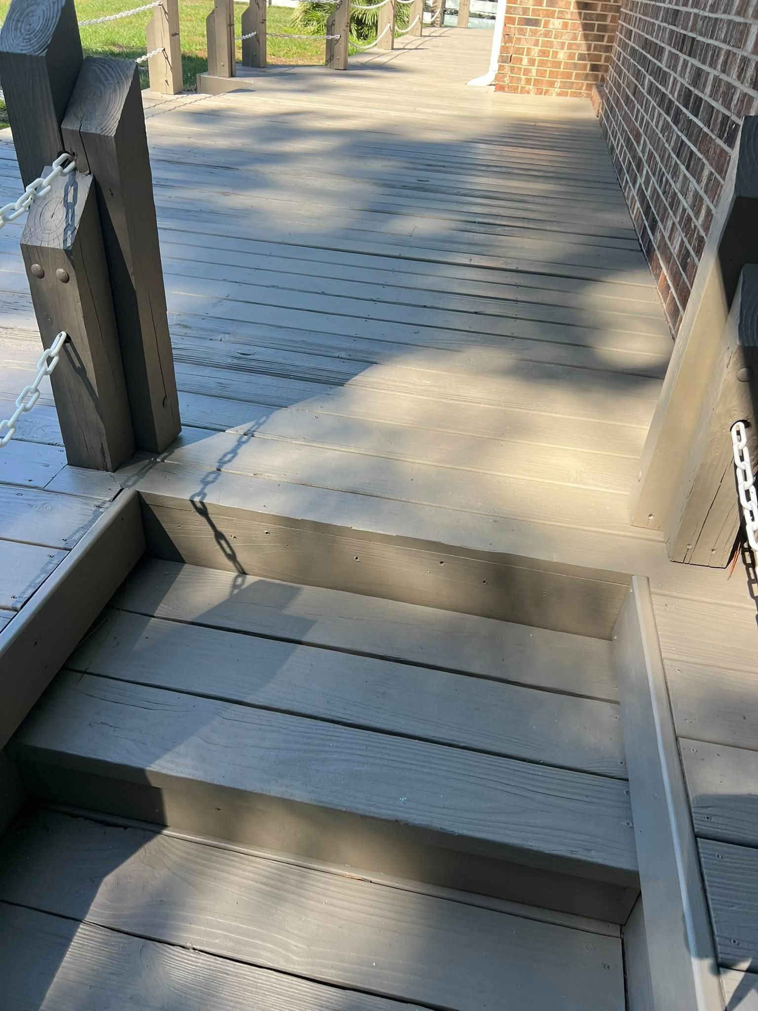Wooden accessibility ramp with textured surface beside a brick building, leading to a sunlit patio.