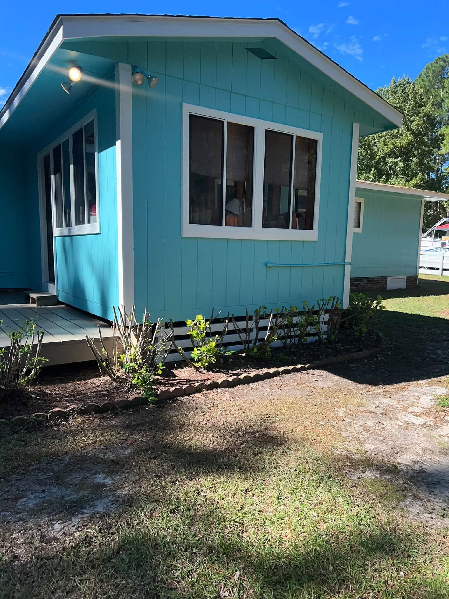 Turquoise house exterior with white-trimmed windows and a small front yard in sunlight