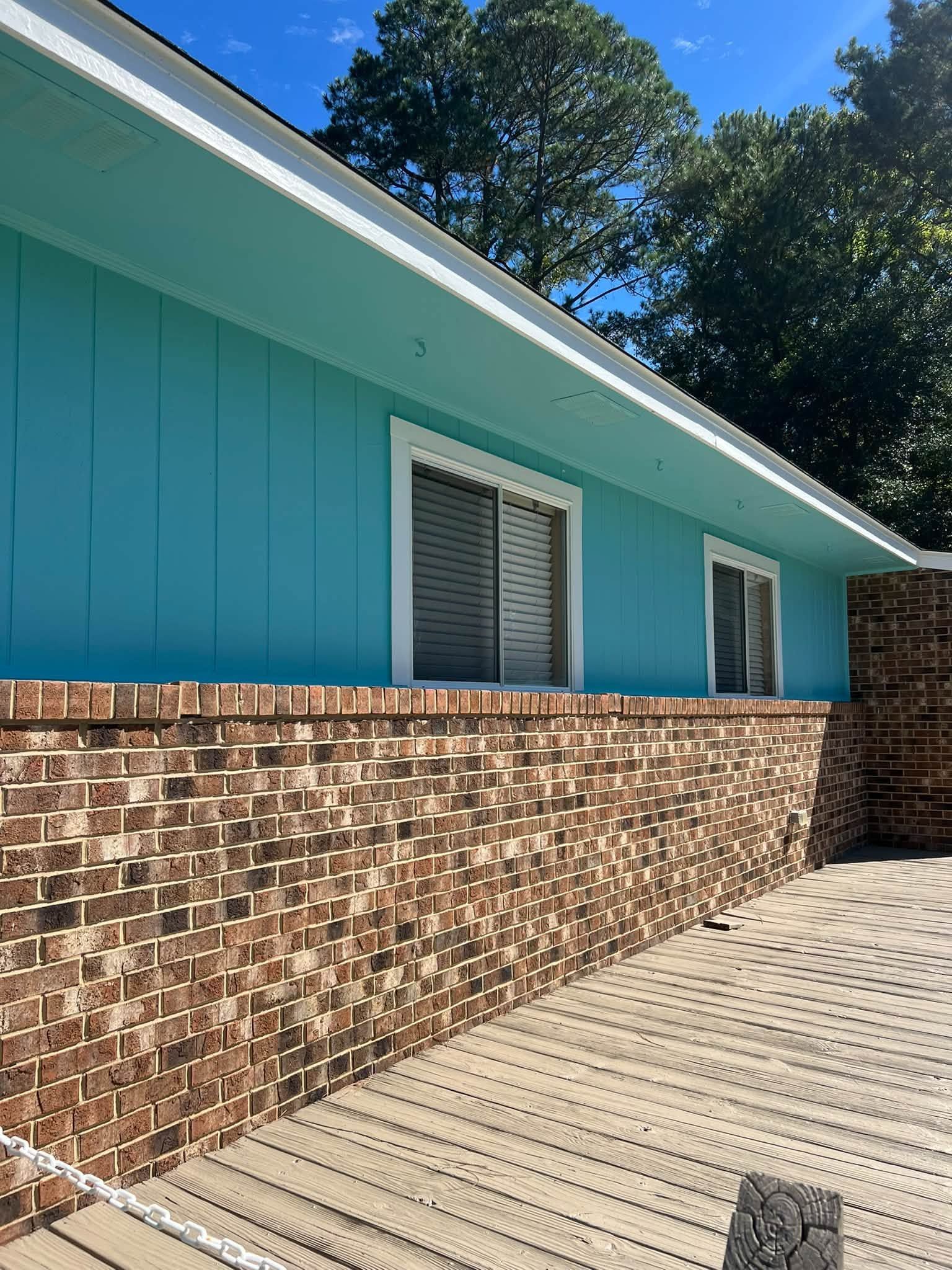 Teal house exterior with brick lower wall, white shutters, and a sunlit concrete driveway
