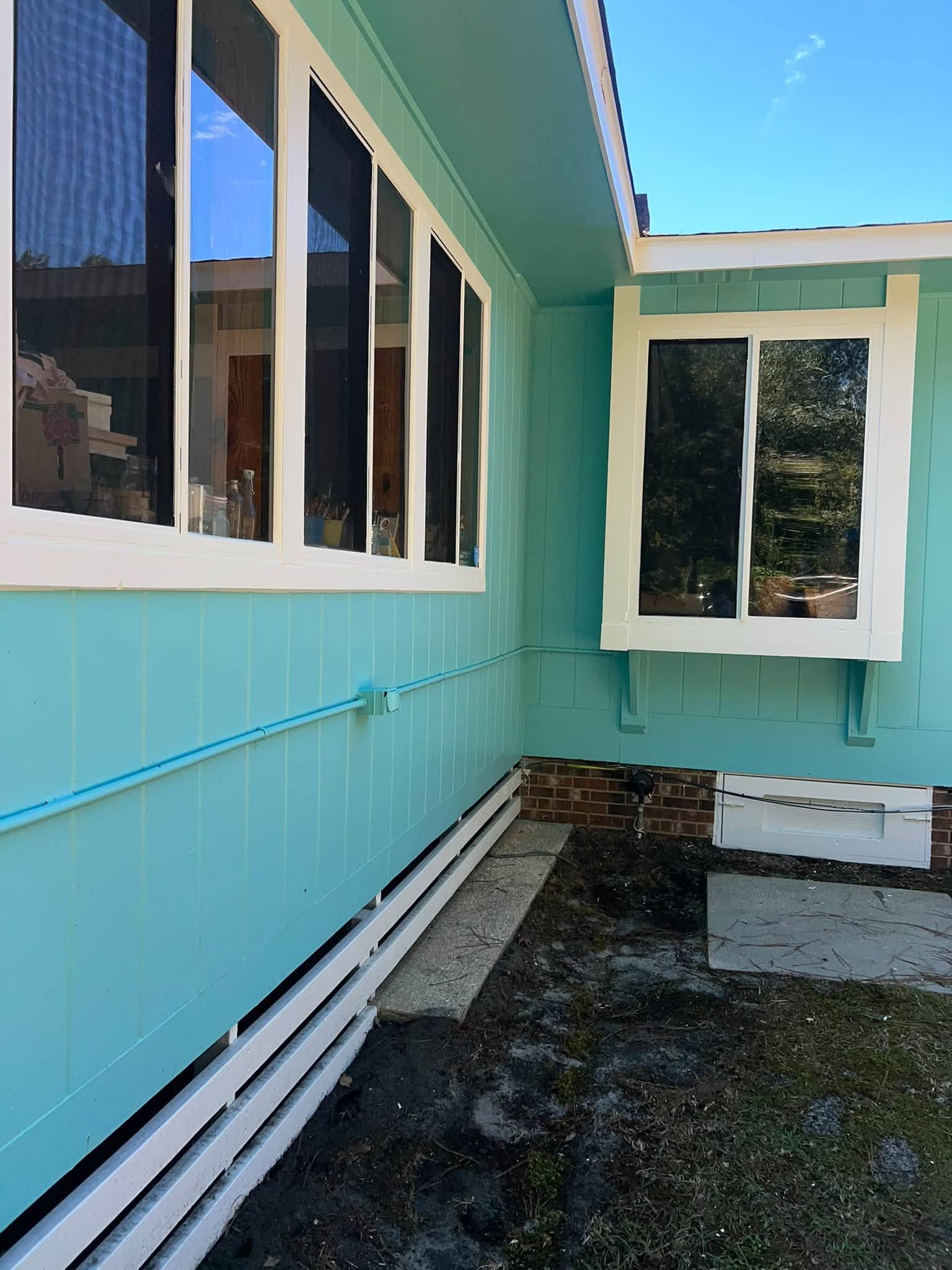 Turquoise house exterior with white-trimmed windows and a small gravel yard under a blue sky