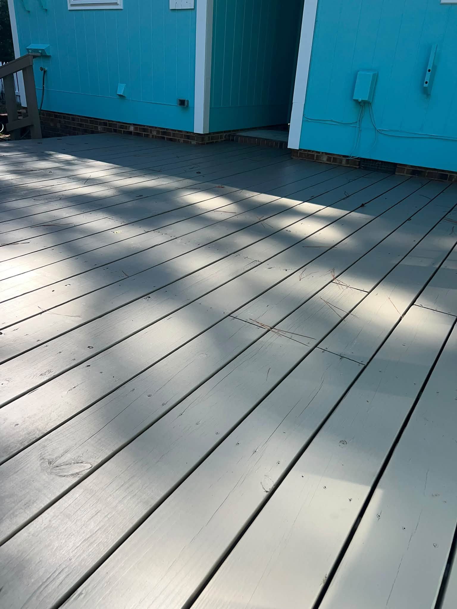 Sunlit gray wooden deck beside bright blue building walls and doors