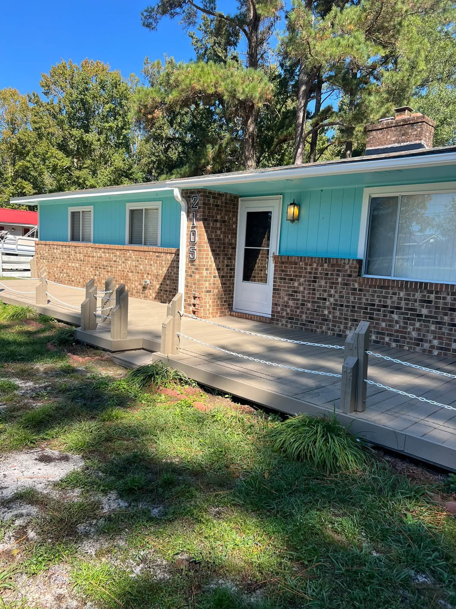Single-story turquoise house with brick facade, white door, and a front porch with ramp and railing