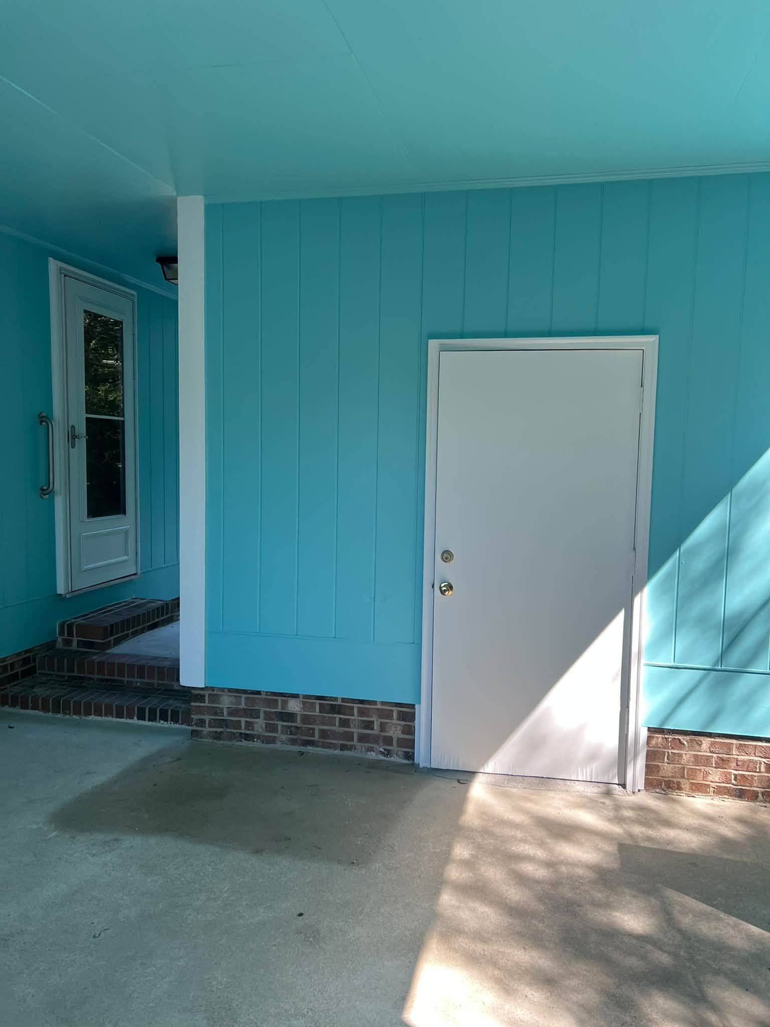 Blue exterior wall with a white door and tiled base outside a shaded porch
