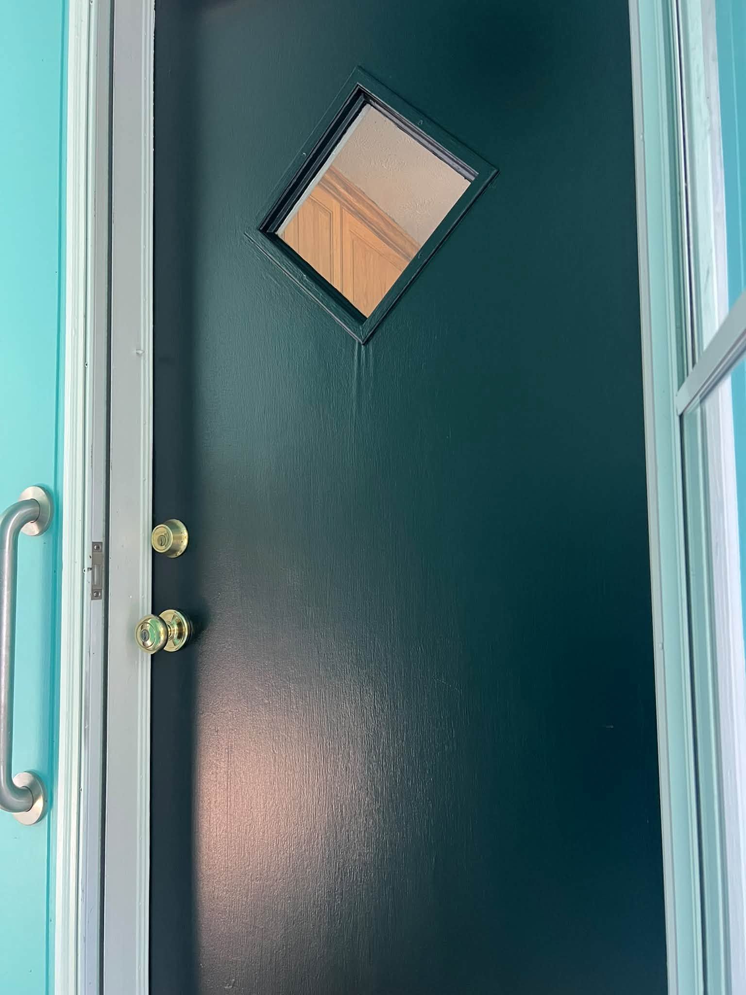 Teal door with a small diamond window and brass handle, seen from a turquoise frame.