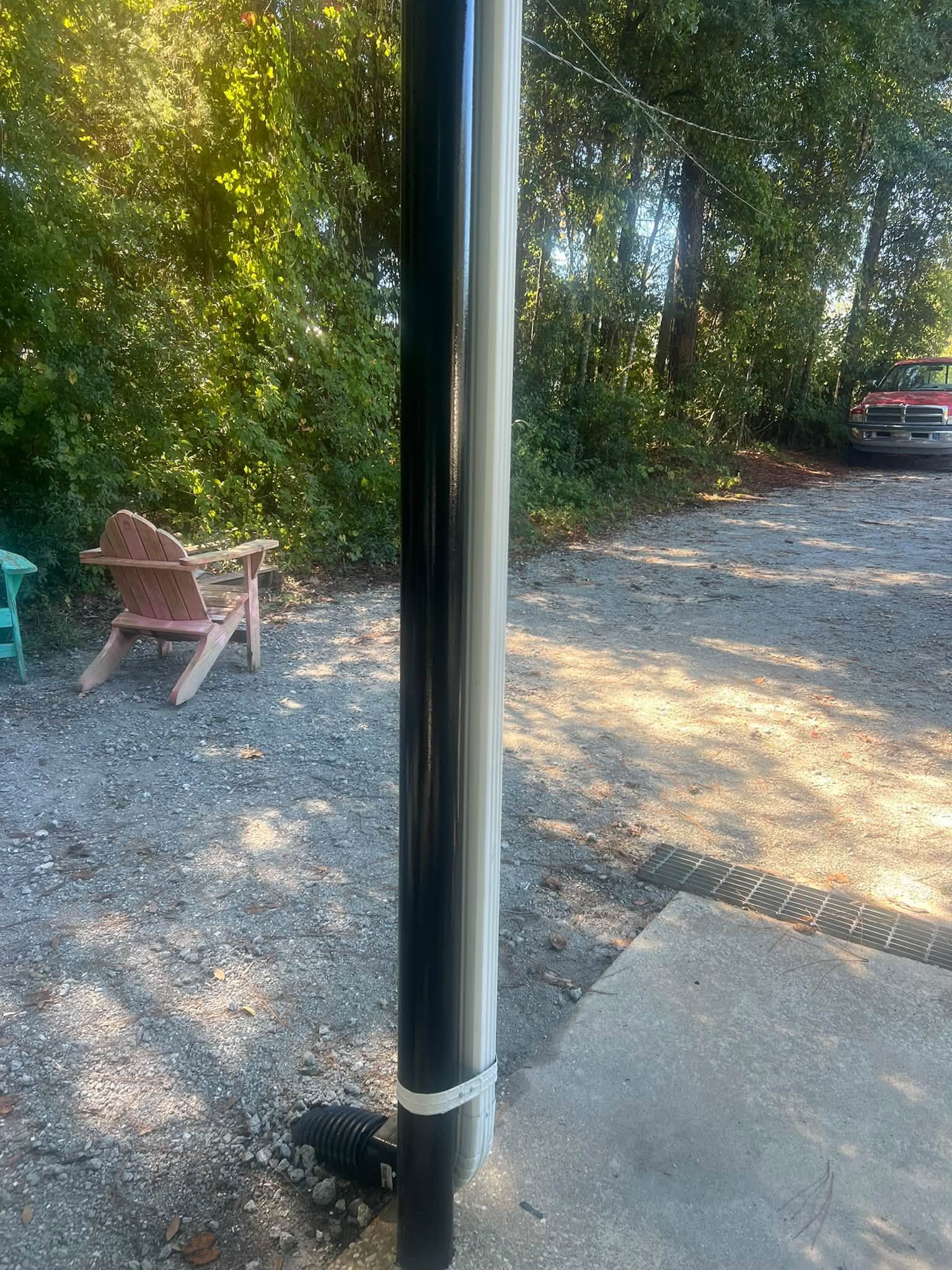 Black pole by gravel driveway, with wooden chair and trees in the background.