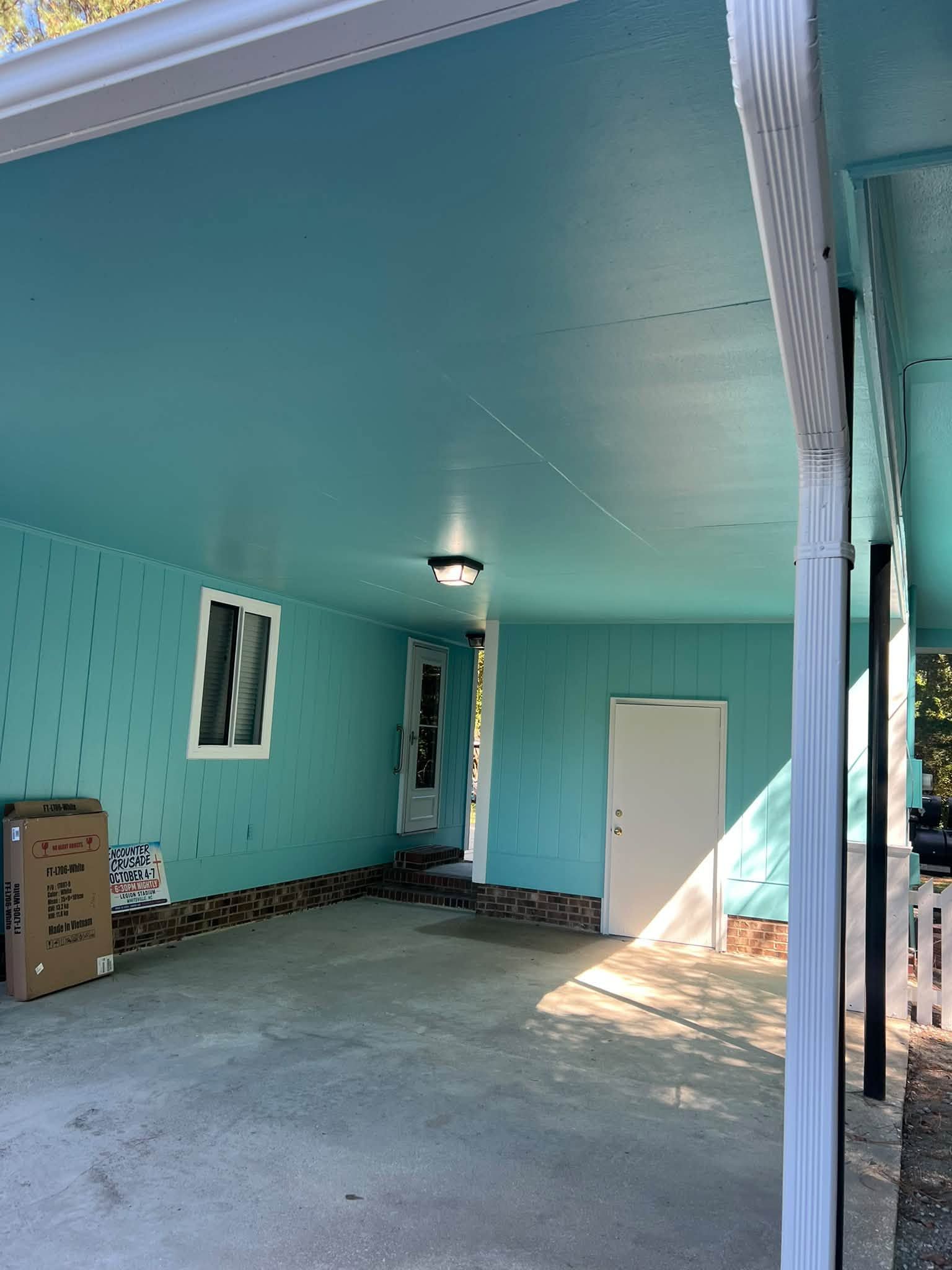 Turquoise covered patio with concrete floor, white door, windows, and a cardboard box on the left.