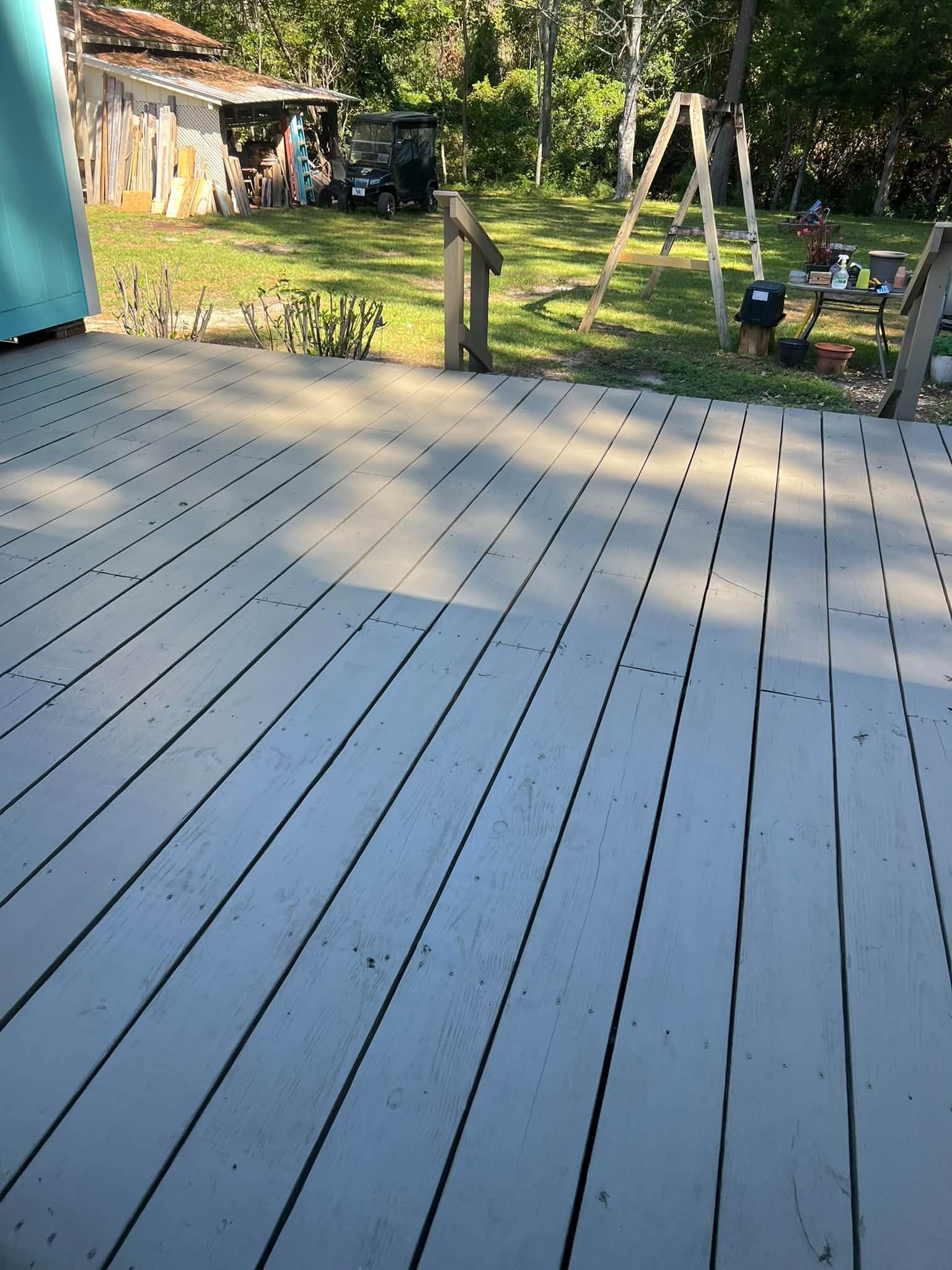 Wooden deck overlooking a sunny backyard with a shed, trees, and a swing set.