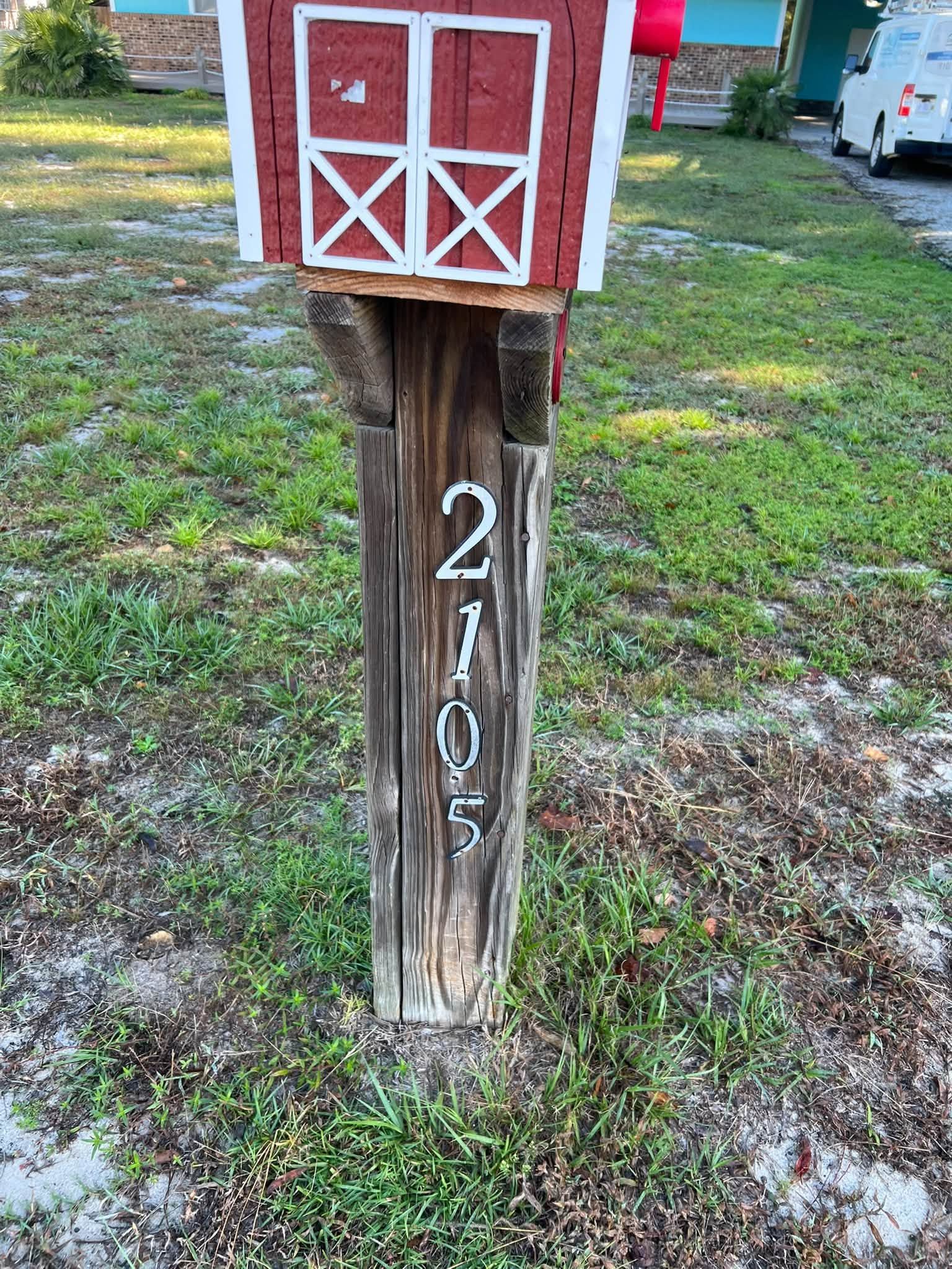Red barn-style mailbox on weathered wooden post marked 2105 in a grassy yard