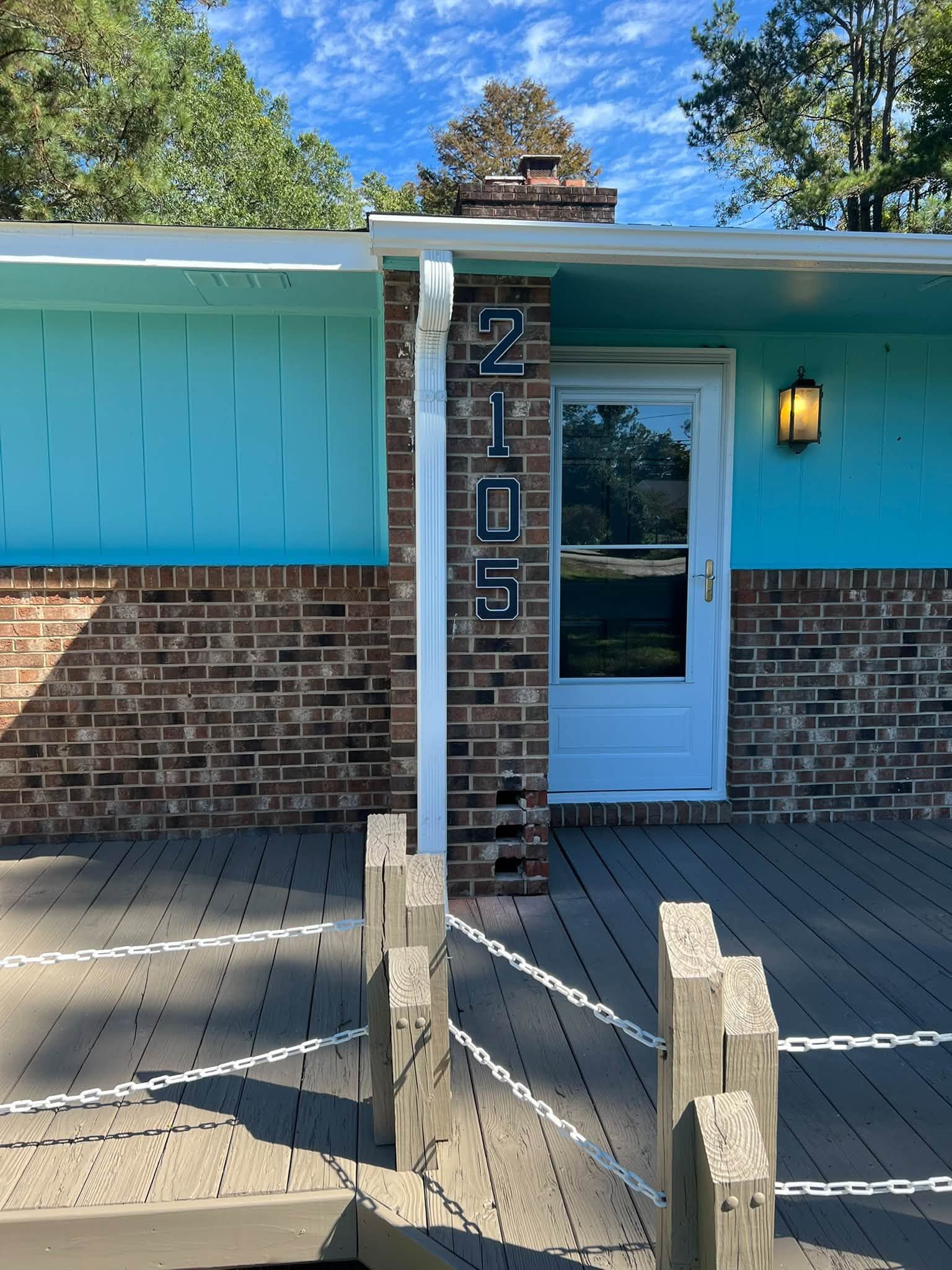 Blue house entrance with brick walls, white door, and vertical address numbers by the porch.