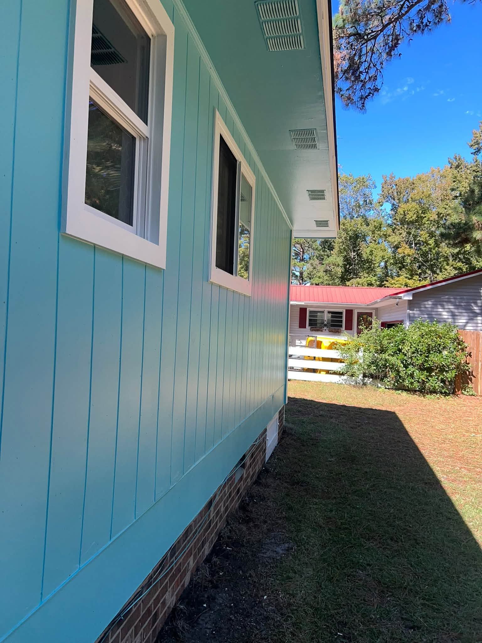 Teal house exterior with white-trimmed windows, grassy yard, and blue sky on a sunny day