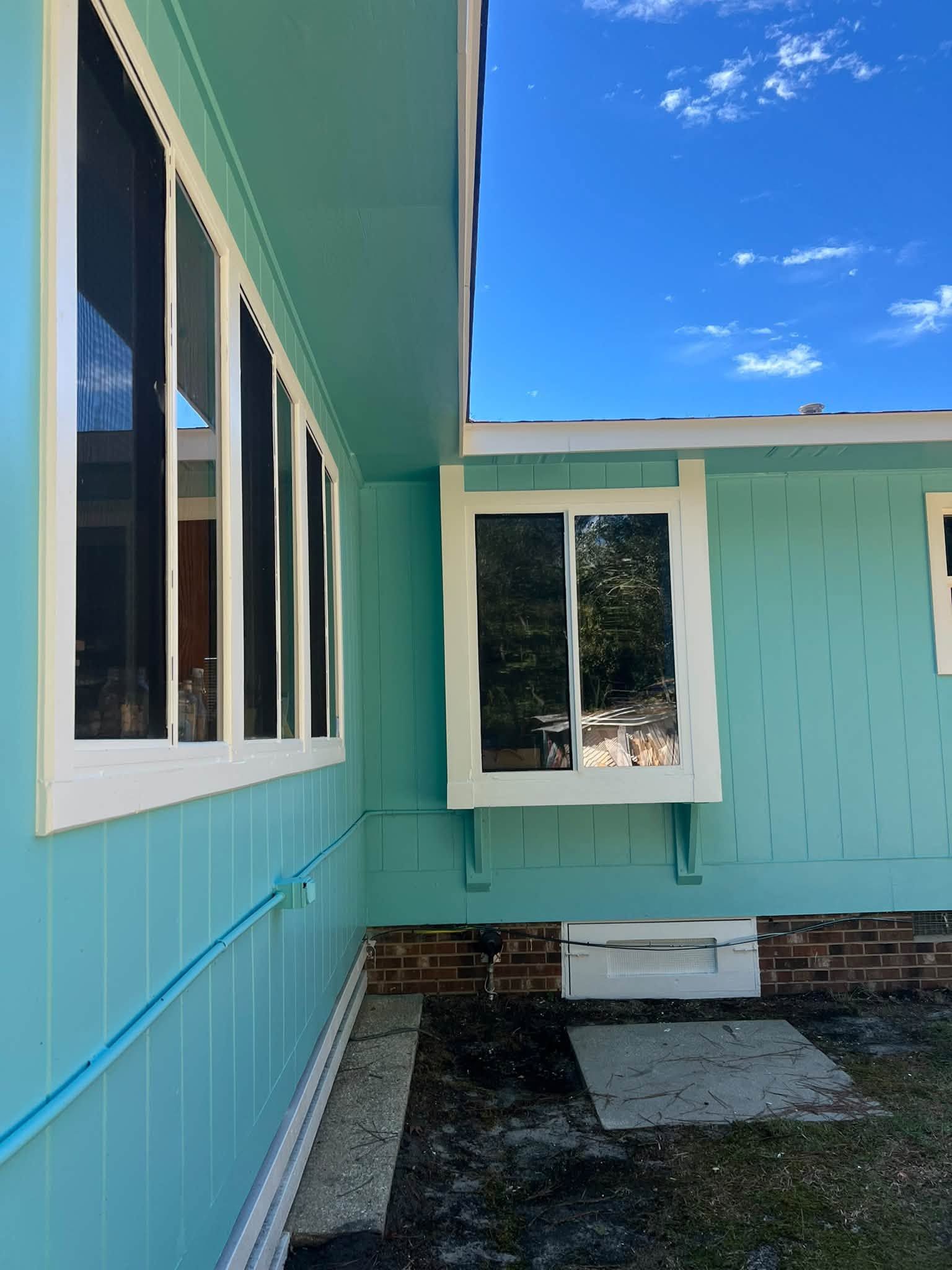 Turquoise house exterior with white-trimmed windows and a small gravel yard under a blue sky