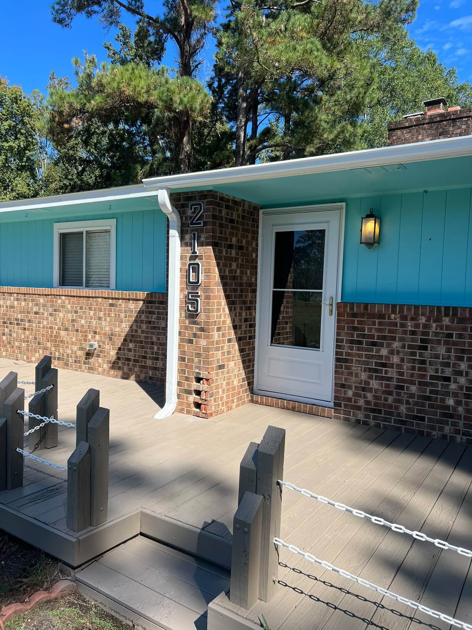 Single-story house with turquoise siding, brick facade, and a white front door behind a fenced patio.