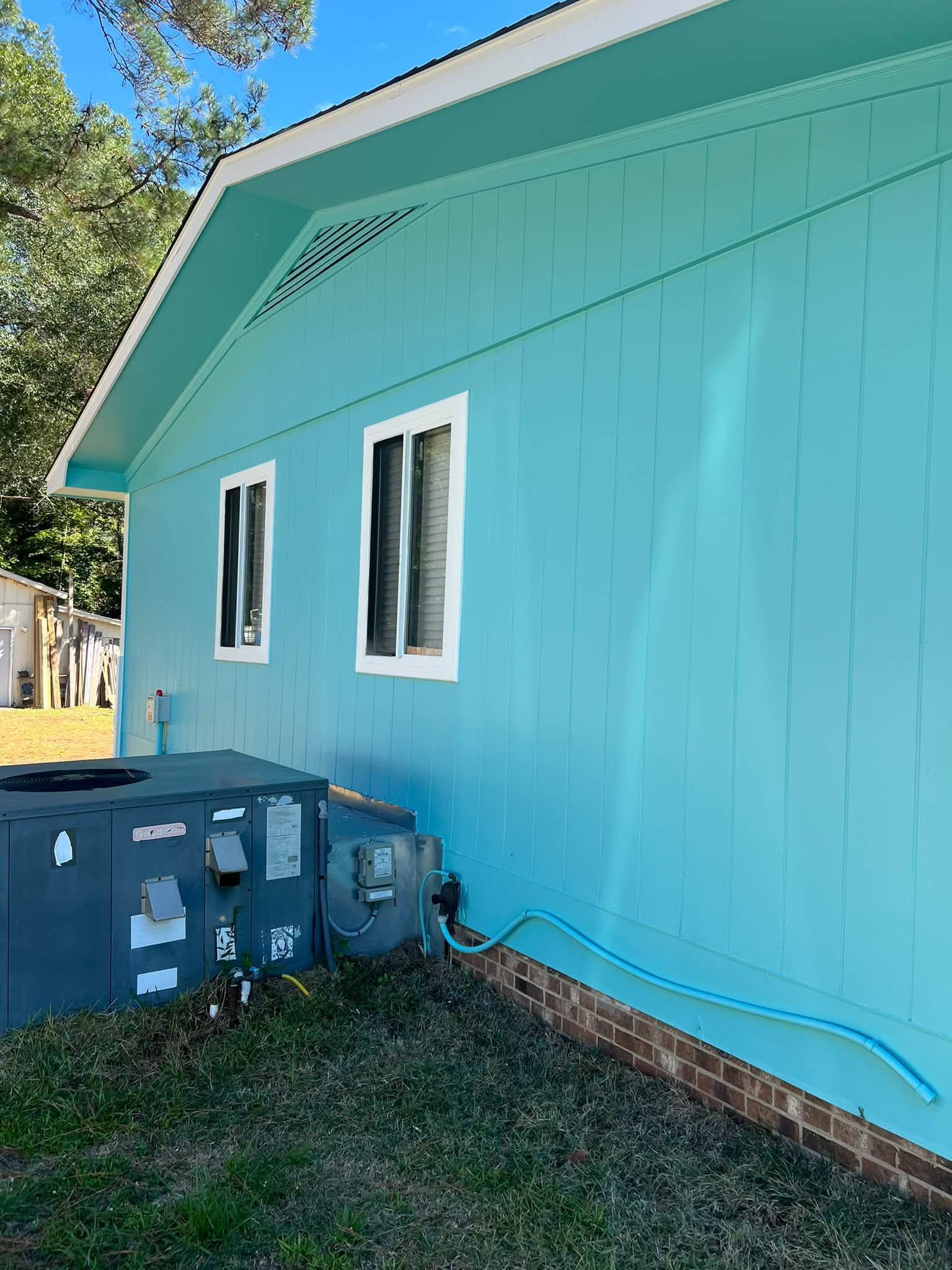 Turquoise house exterior with two windows, blue utility boxes, and a grassy yard