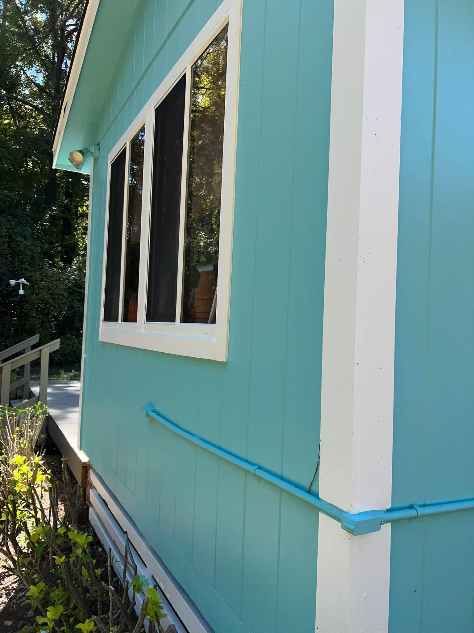 Turquoise house exterior with white-trimmed windows and blue handrail beside a garden path
