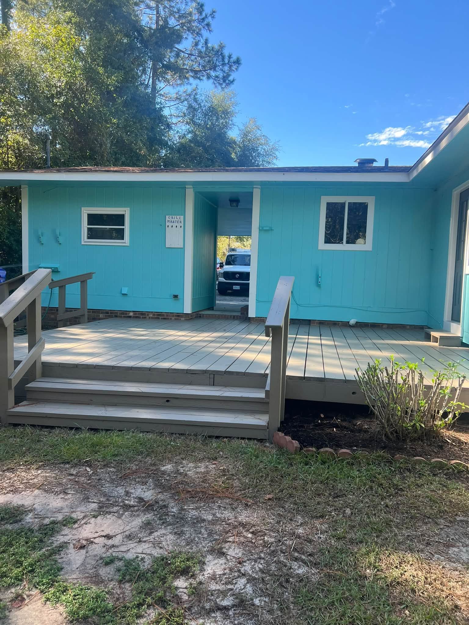 Turquoise house exterior with white trim, open door, and a wooden front porch under a blue sky