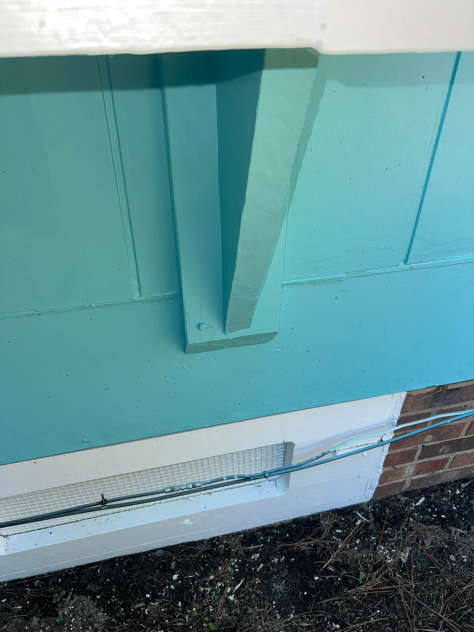 Turquoise-painted exterior wall with a metal support beam and white trim above a brick foundation.