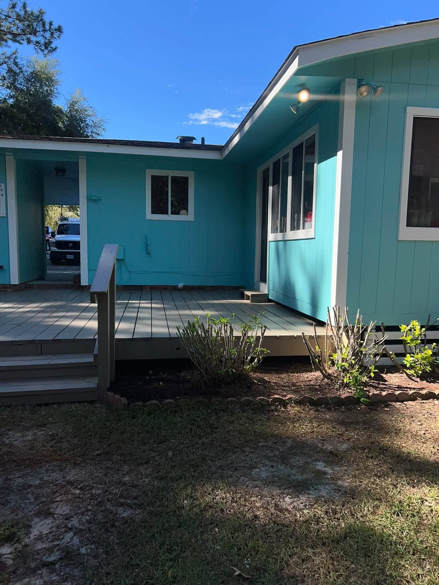 Turquoise house exterior with front steps, porch, and white-trimmed windows under a blue sky