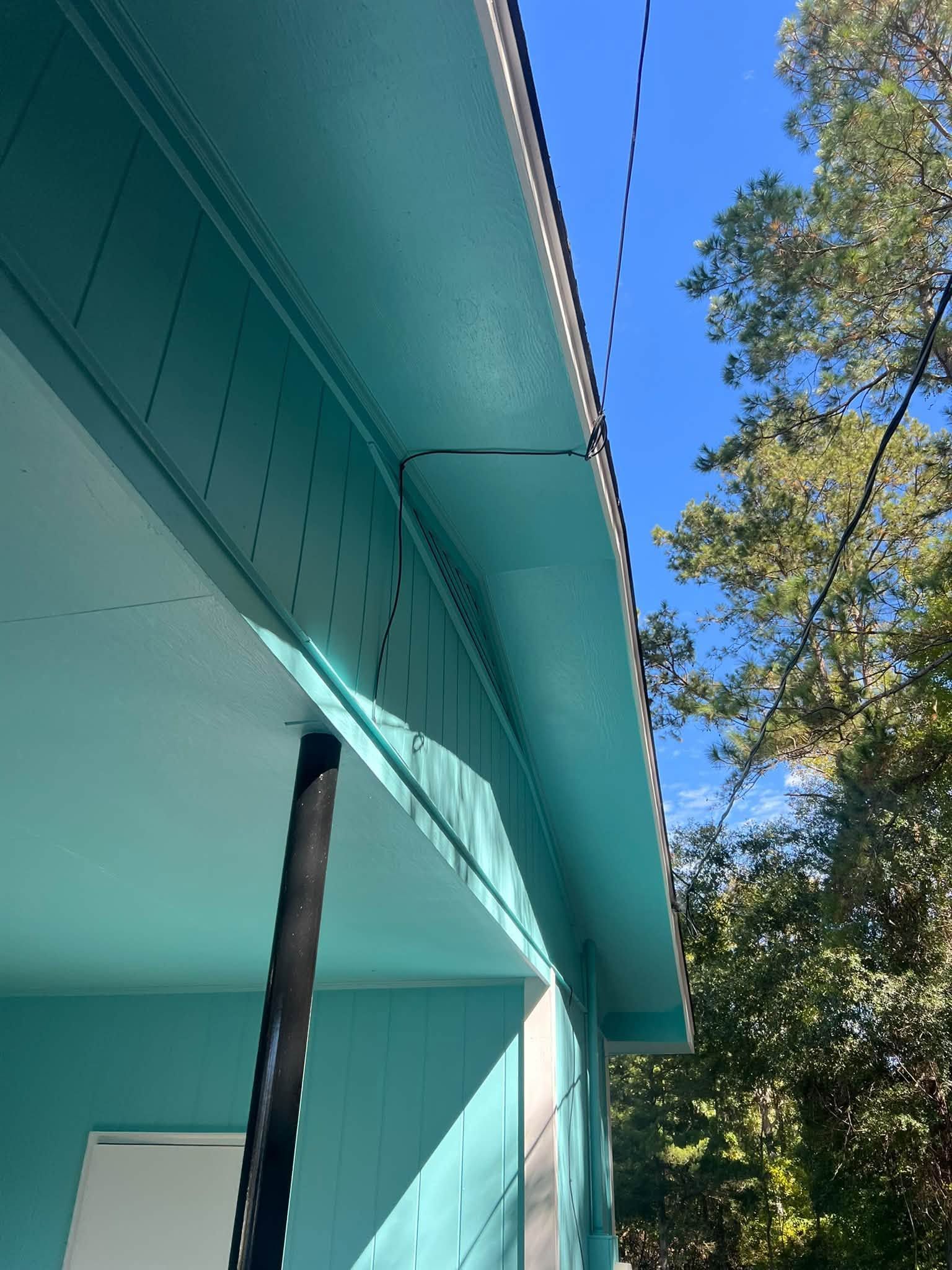 Turquoise house eaves and porch corner against a blue sky with trees.
