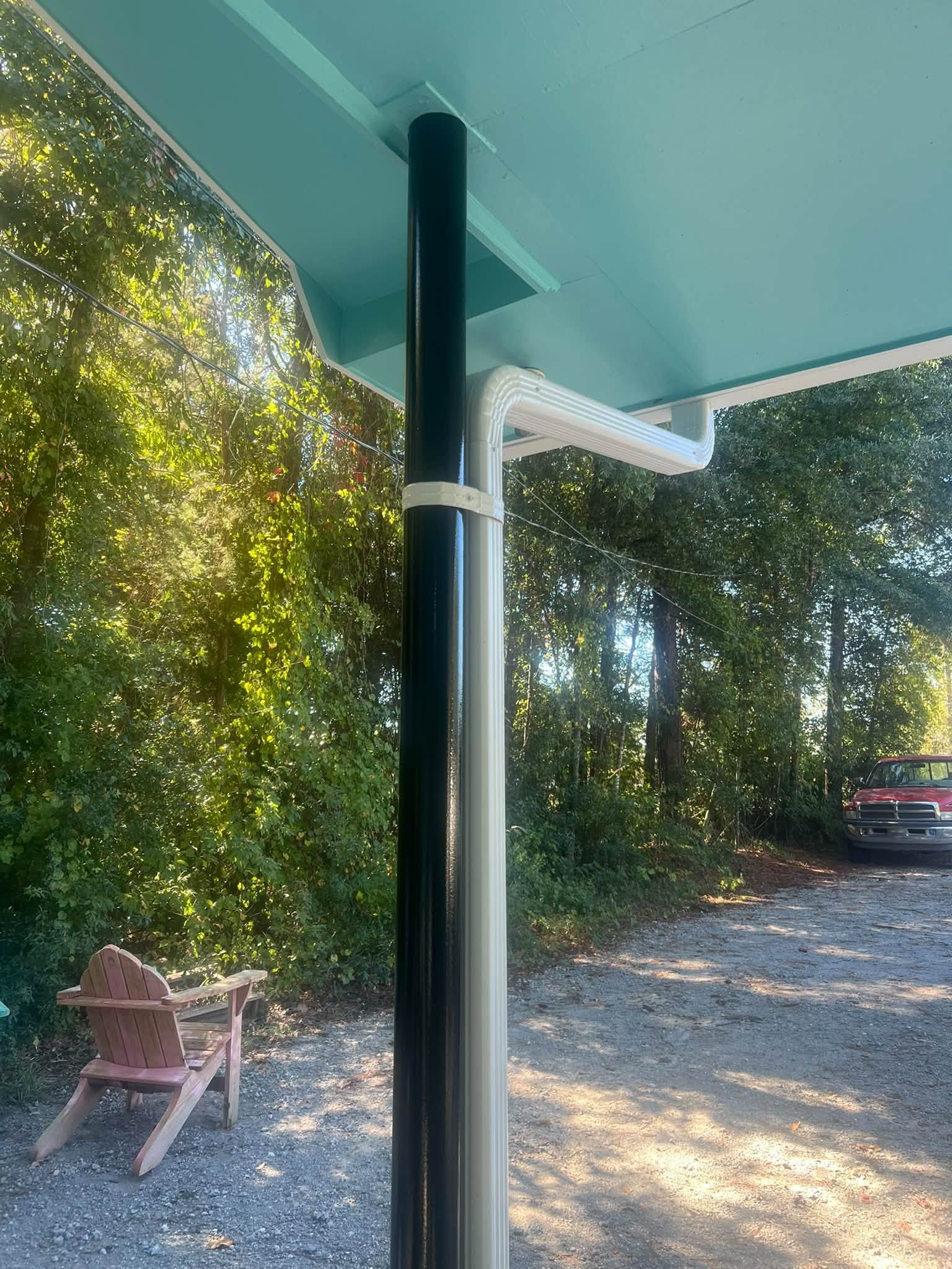 Covered porch with a dark post beside a gravel driveway, trees, a bench, and a parked car in the background