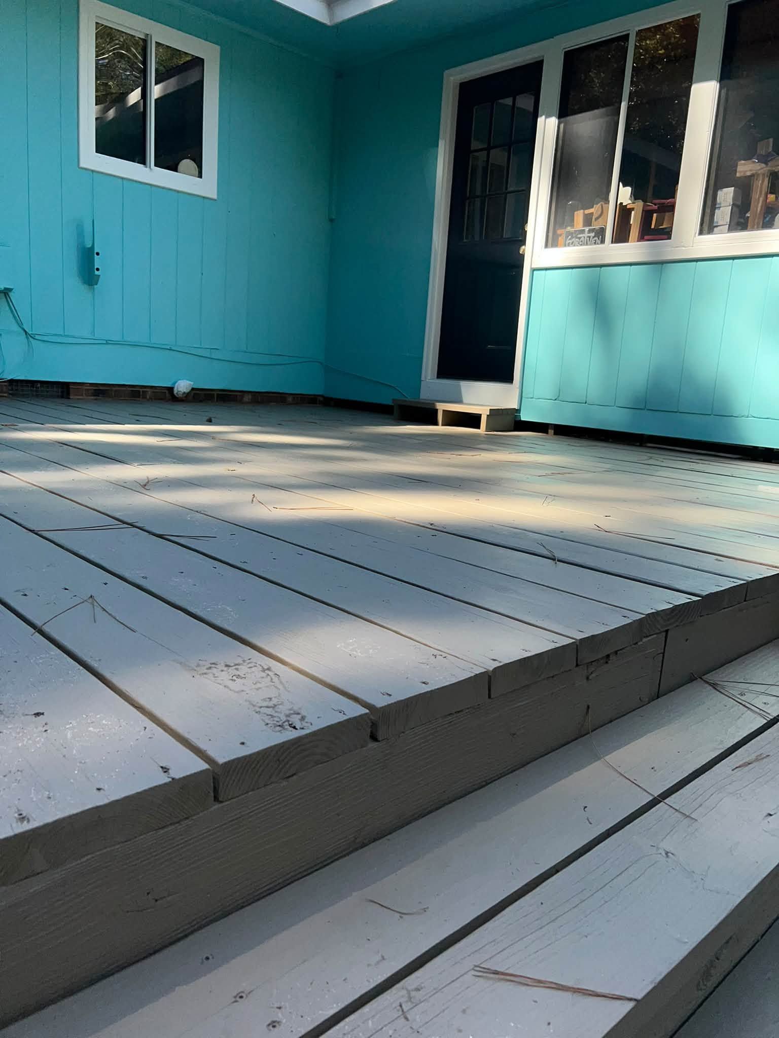 Turquoise house porch with white deck steps and a glass door in sunlight