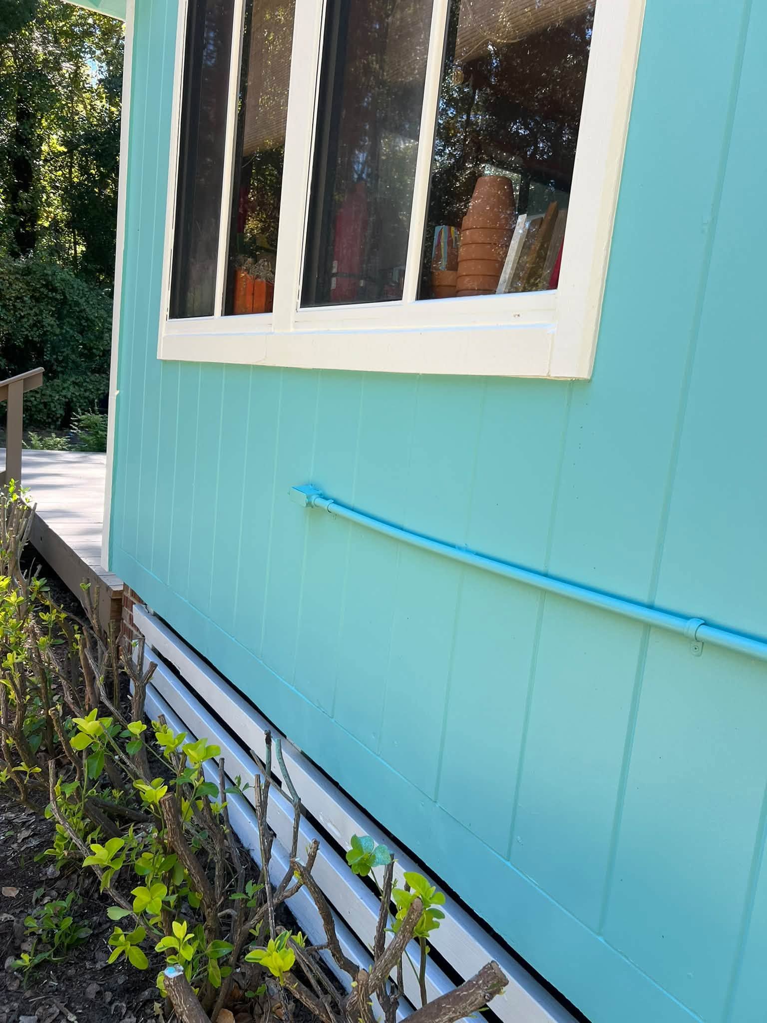 Turquoise house wall with white-trimmed window, blue handrail, and plants along a narrow side path