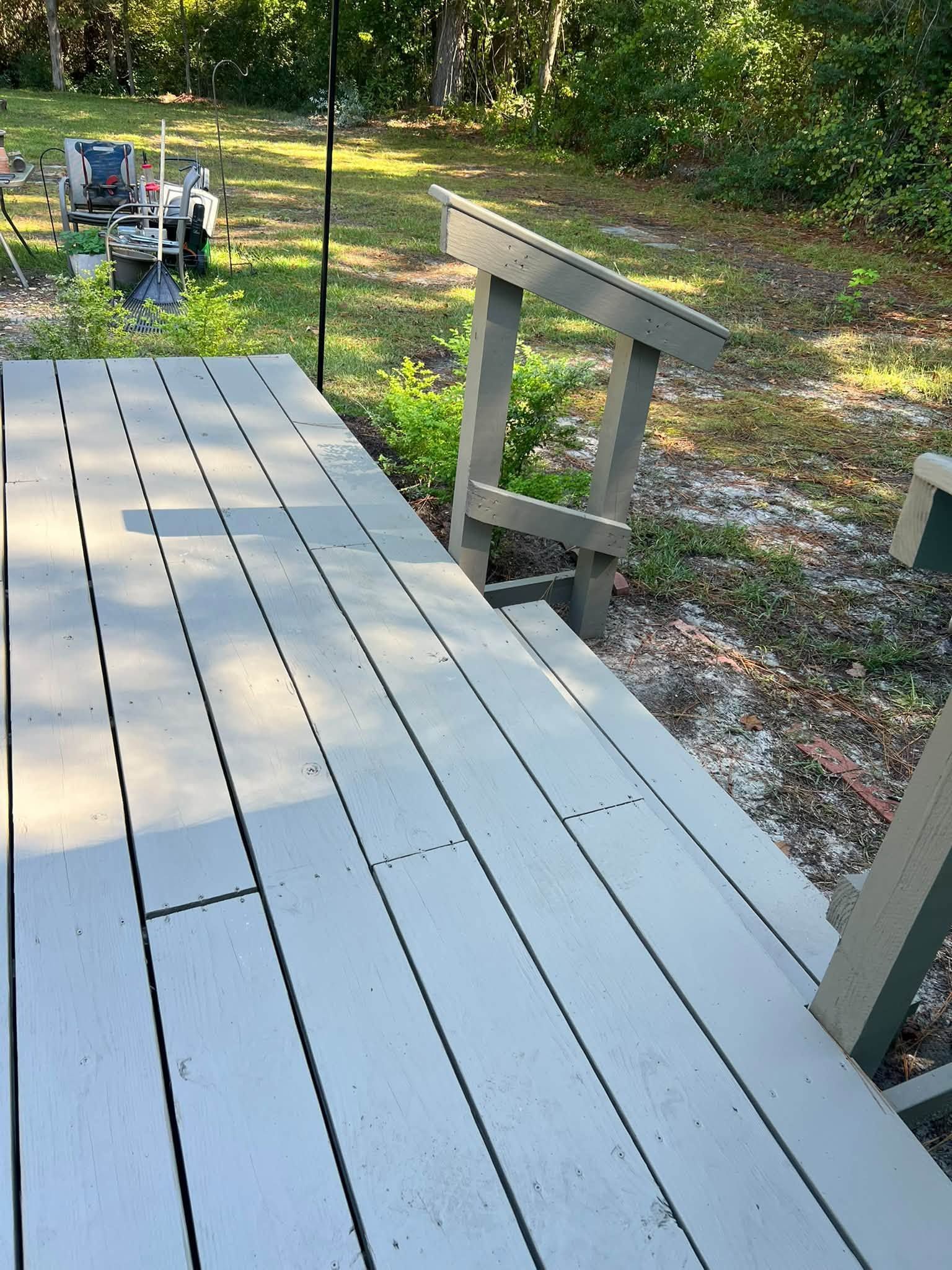 White deck railing overlooking a wooded yard, with a lawn mower in the distance.