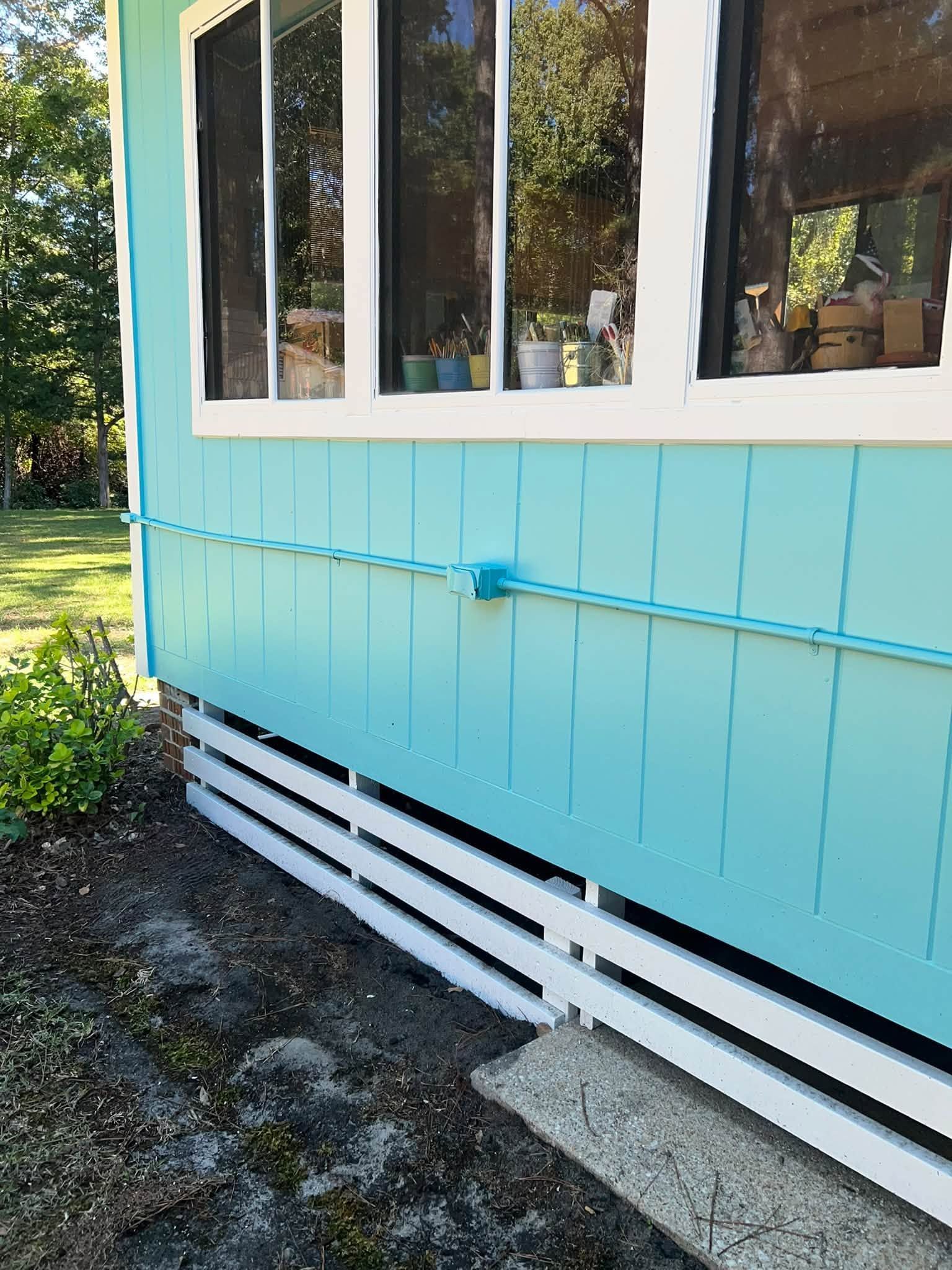 Exterior of a turquoise house with windows, white trim, and horizontal skirting above a gravel path