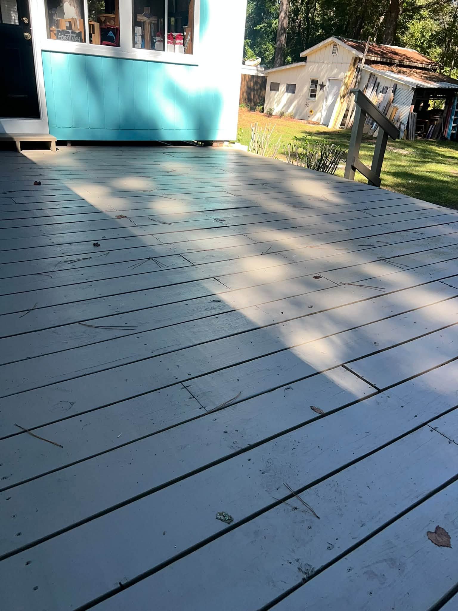 Blue-gray deck in sunlight beside a turquoise house, with tree shadows and a yard in the background