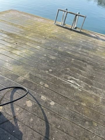 Weathered wooden dock beside calm water with a metal ladder and a black hose on the deck.