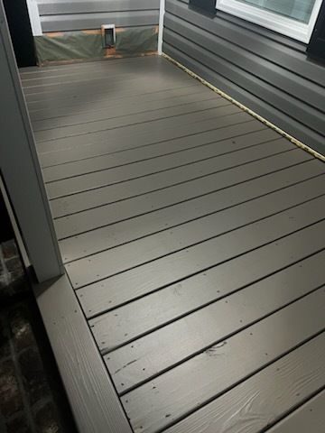 Empty gray wooden deck beside a house, with railing and wall siding.