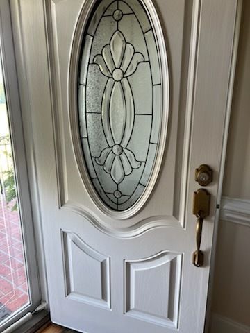 White front door with oval frosted glass panel and brass handle, viewed from inside near a side window