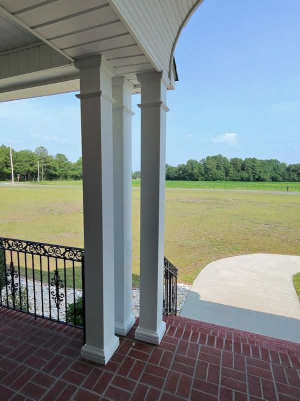 Porch overlooking a grassy field and tree line under a clear blue sky