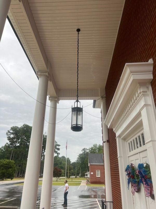 Covered porch with hanging lantern, white columns, wet pavement, and a person walking in the rain outside.