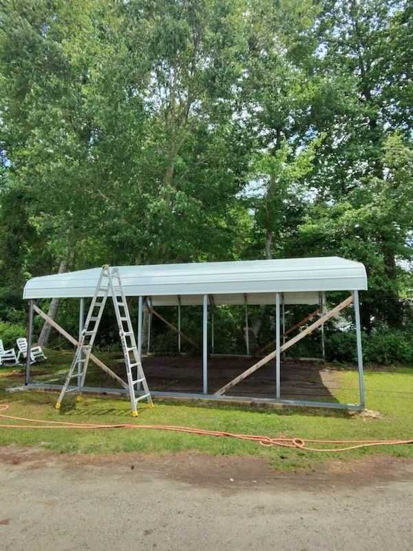 White canopy shelter under construction, with ladders and support braces in a grassy wooded area