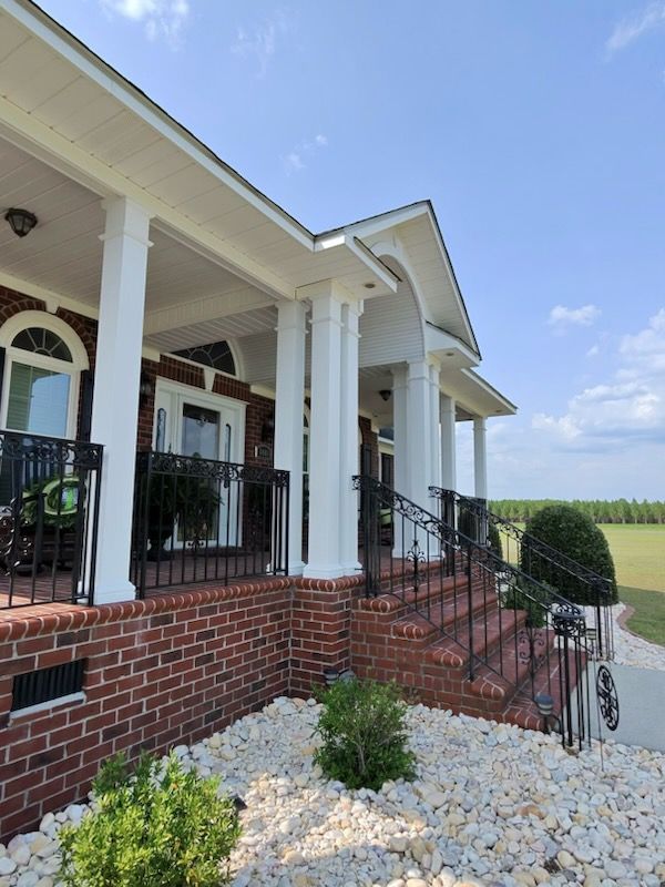 Brick porch with white columns, black railings, and steps leading to a home under a blue sky.