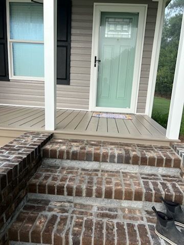 Front porch with brick steps, white columns, and a light green front door on a beige house.