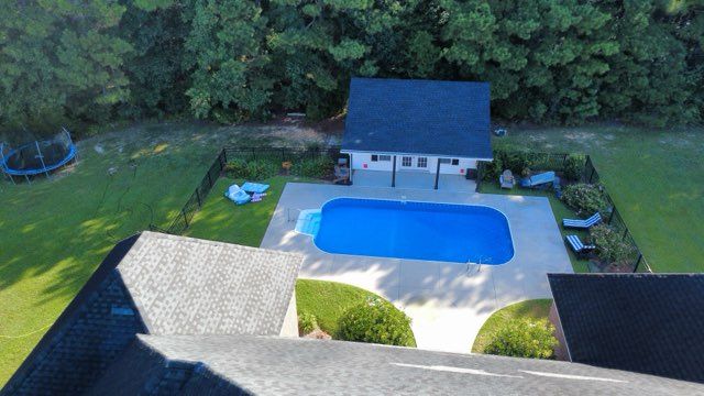 Aerial view of a backyard with a blue swimming pool beside a small house and surrounding trees