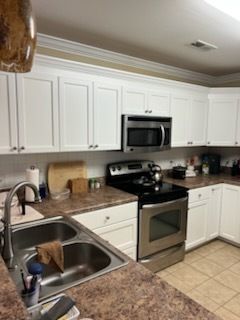 Bright white kitchen with stainless steel appliances, brown countertops, and a double sink.