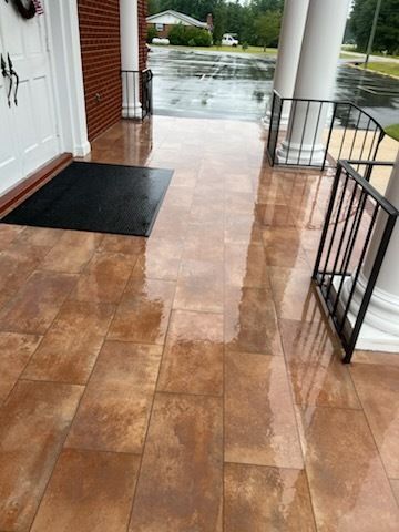 Covered porch with wet tiled floor, black mats, and rain-soaked driveway beyond the railing