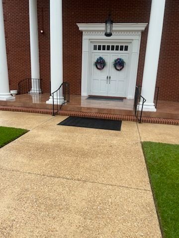 Front entrance with white double doors, brick columns, black railing, and a concrete walkway.