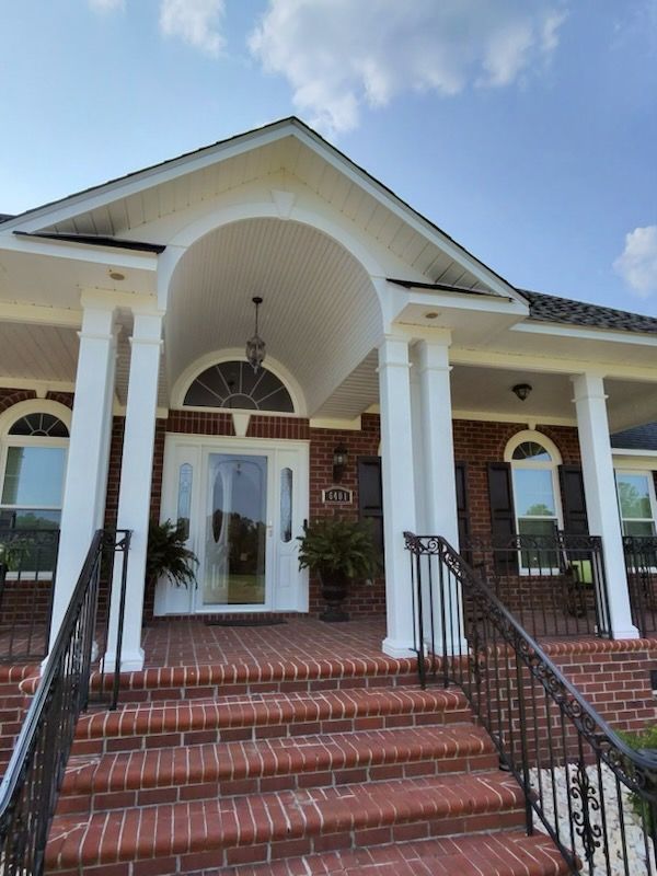 Brick house entrance with white columns, arched porch, and red-tiled steps leading to the front door.